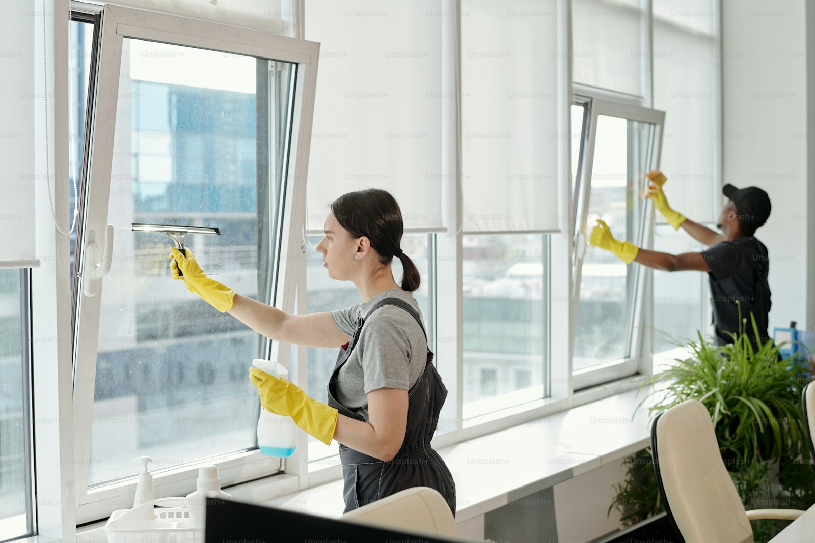 Professional cleaner in workwear cleaning a glass surface in a modern office
